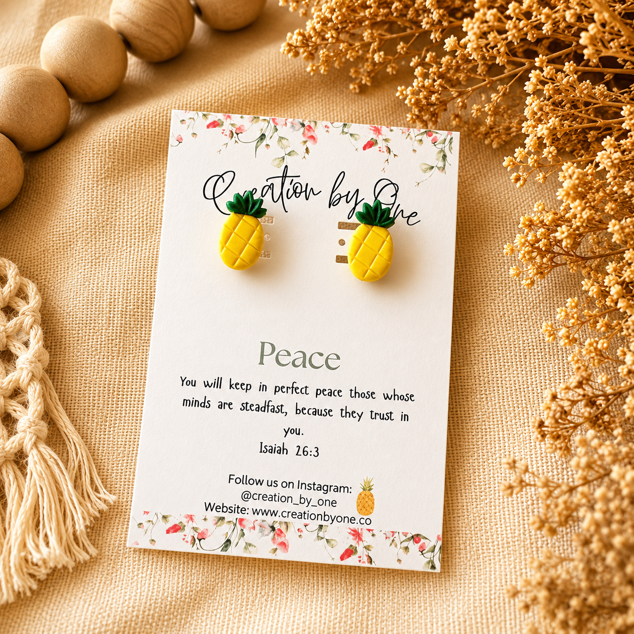 Pineapple-shaped earrings on a 'Creation by One' branded card with decorative elements on a beige surface.