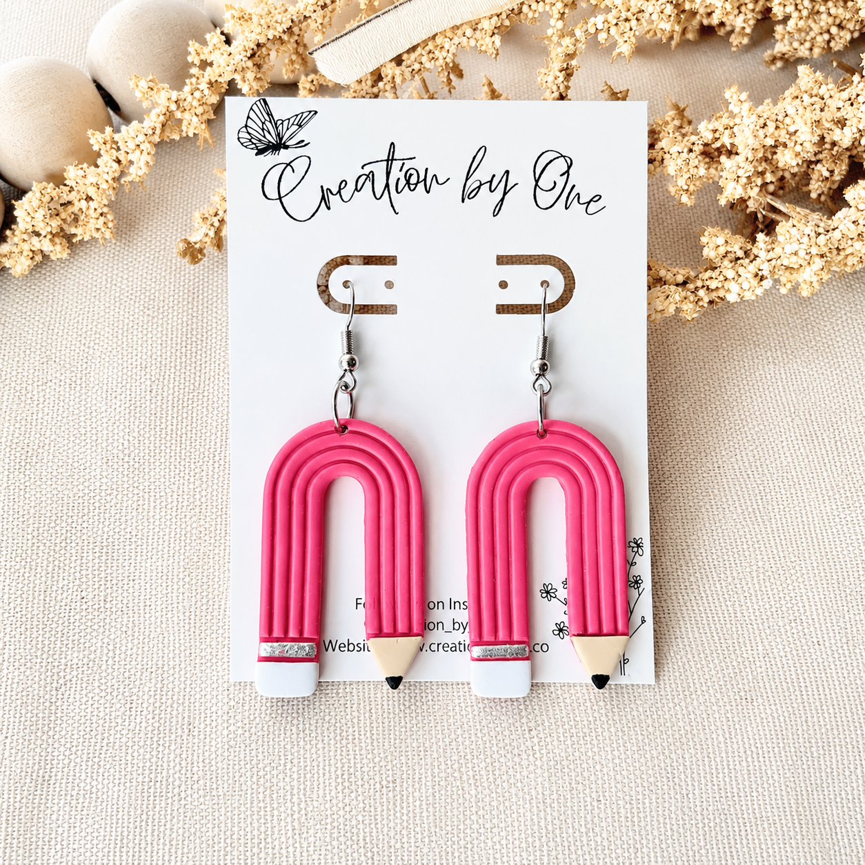 Pink arch-shaped earrings on a card with 'Creation by One' branding, surrounded by decorative elements.