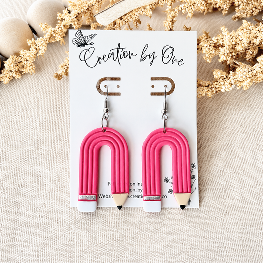 Pink arch-shaped earrings on a card with 'Creation by One' branding, surrounded by decorative elements.