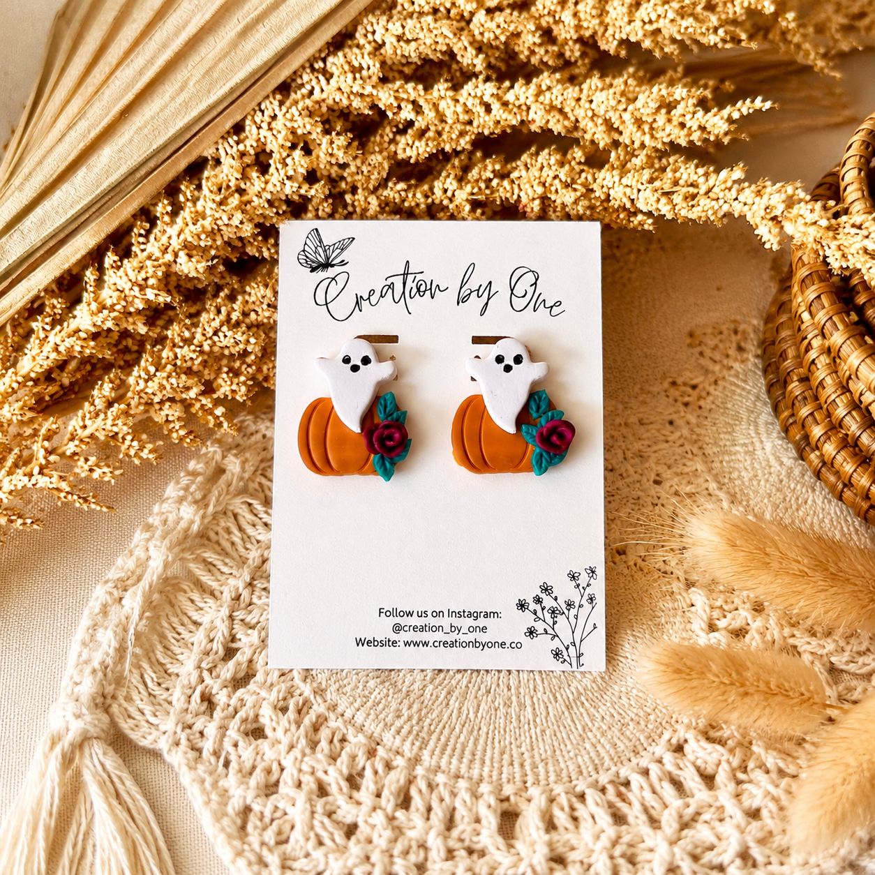 Pair of ghost and pumpkin earrings on a 'Creation by One' branded card with decorative elements.