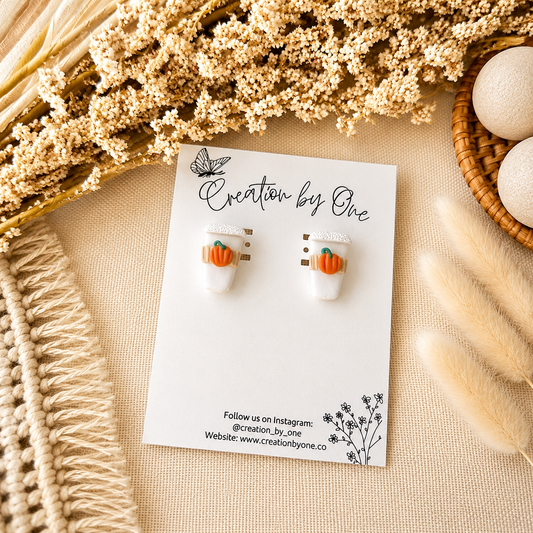 Pair of pumpkin earrings on a 'Creation by One' branded card with decorative elements.