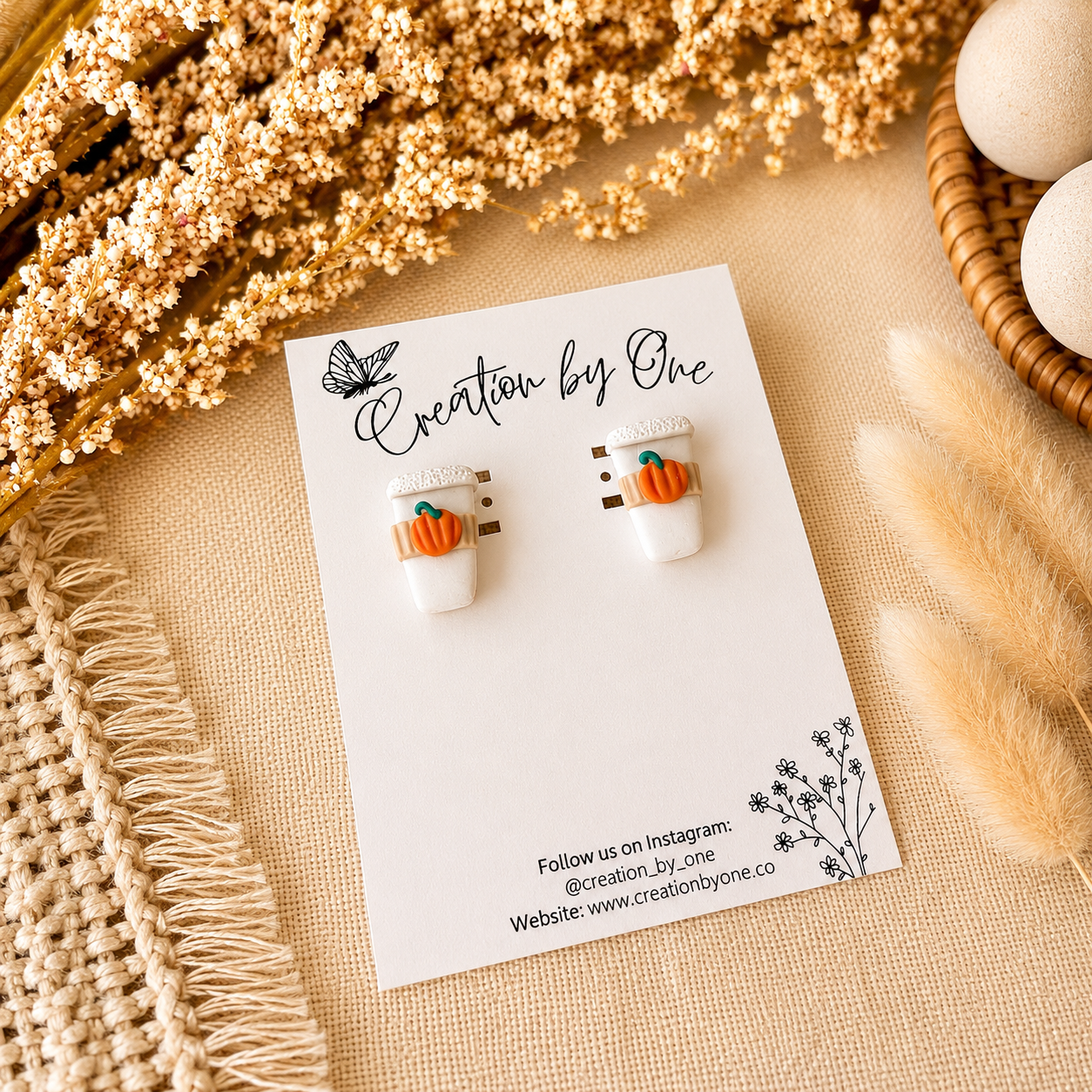 Pair of earrings on a card with 'Creation by One' branding, surrounded by decorative elements.