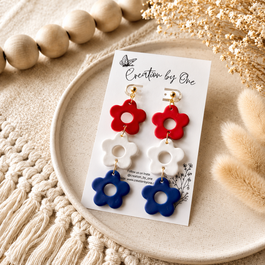 Flower-shaped earrings on a card with 'Creation by One' branding, placed on a textured surface.