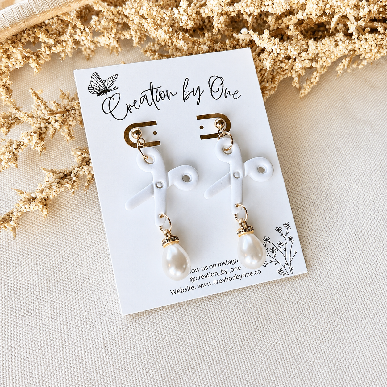 Pair of earrings on a 'Creation by One' branded card with decorative elements.