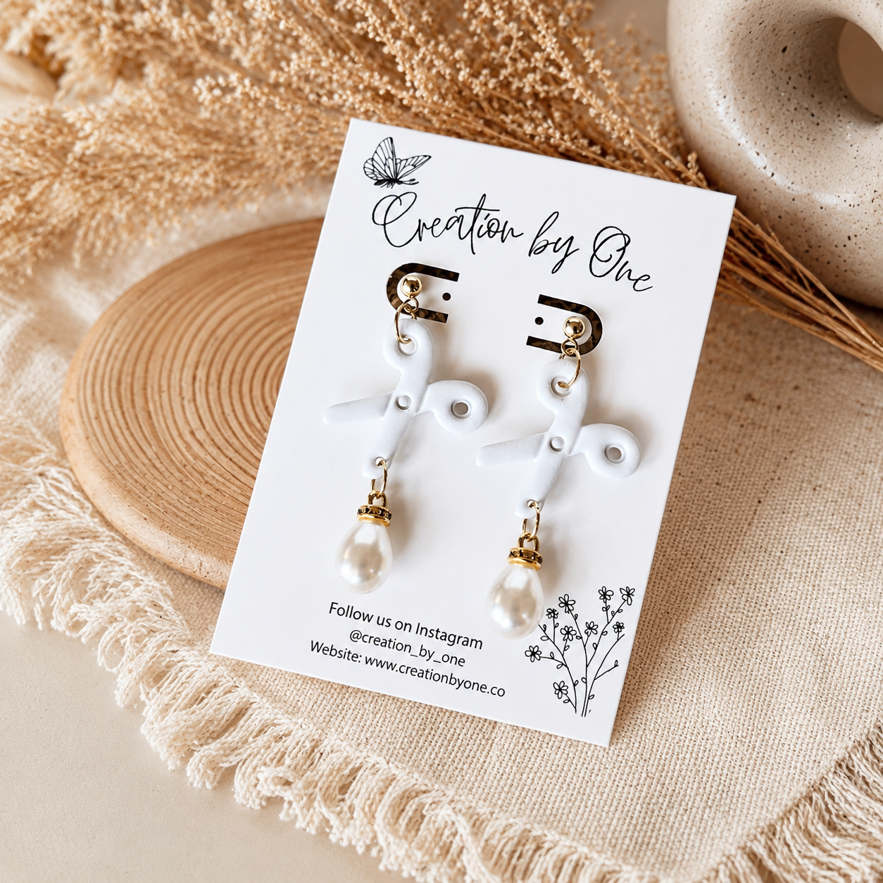 Pair of earrings on a 'Creation by One' branded card with decorative elements.