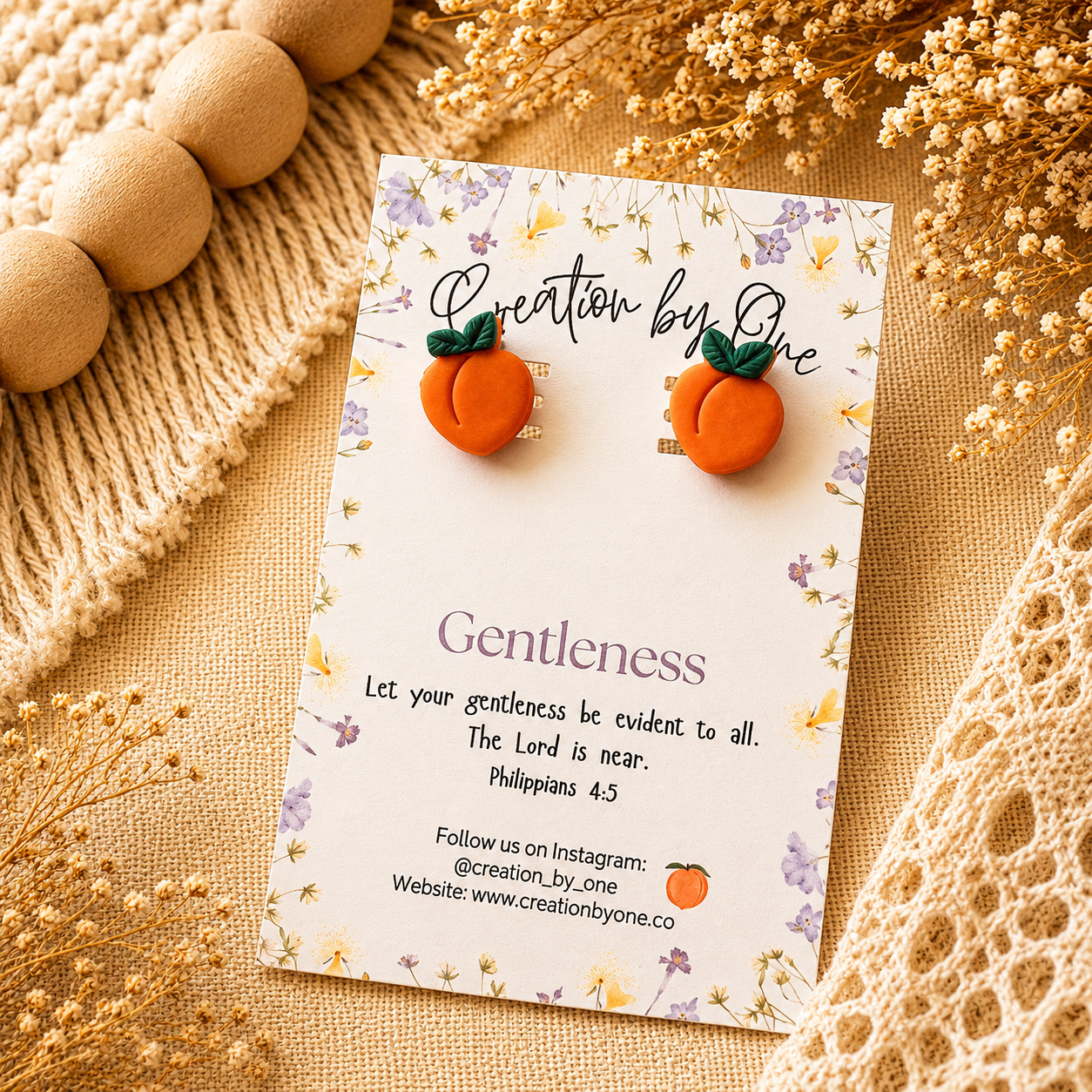 Orange pumpkin-shaped earrings on a 'Creation by One' branded card with decorative elements.