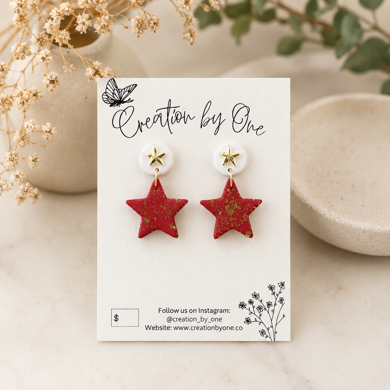Red star-shaped earrings on a 'Creation by One' branded card with decorative elements.