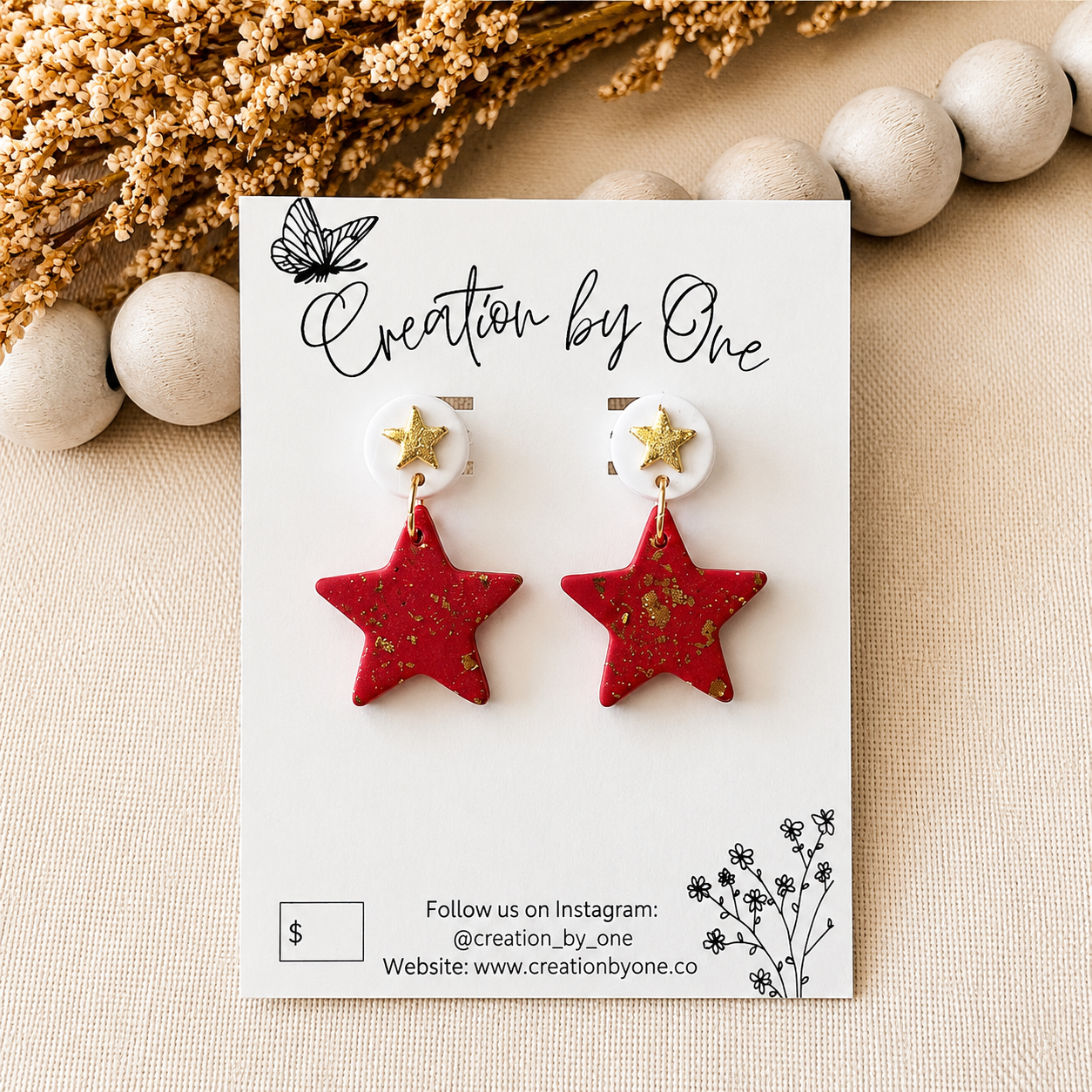 Red star-shaped earrings on a 'Creation by One' branded card with decorative elements.