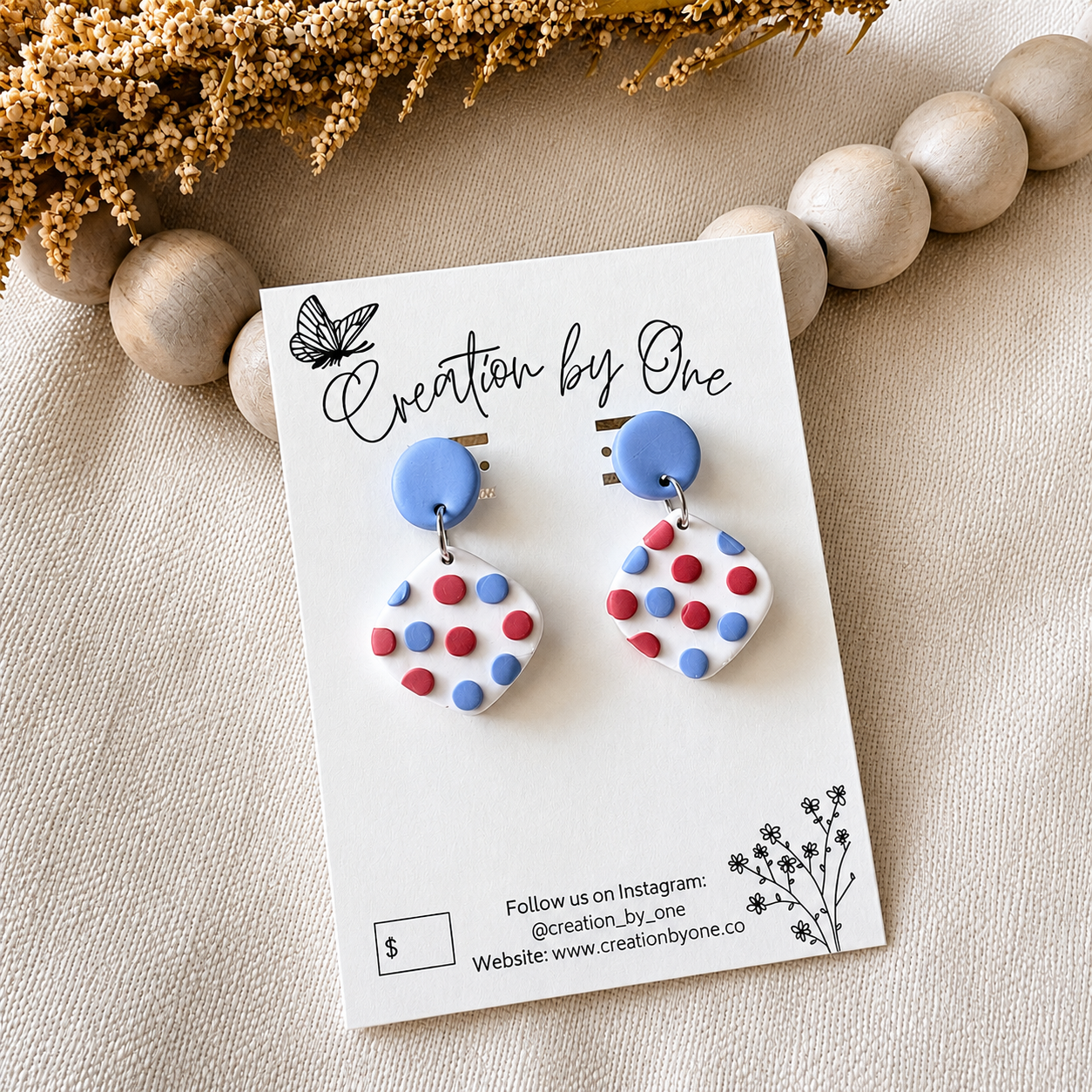 Heart-shaped earrings with blue and multicolored polka dots on a 'Creation by One' branded card.