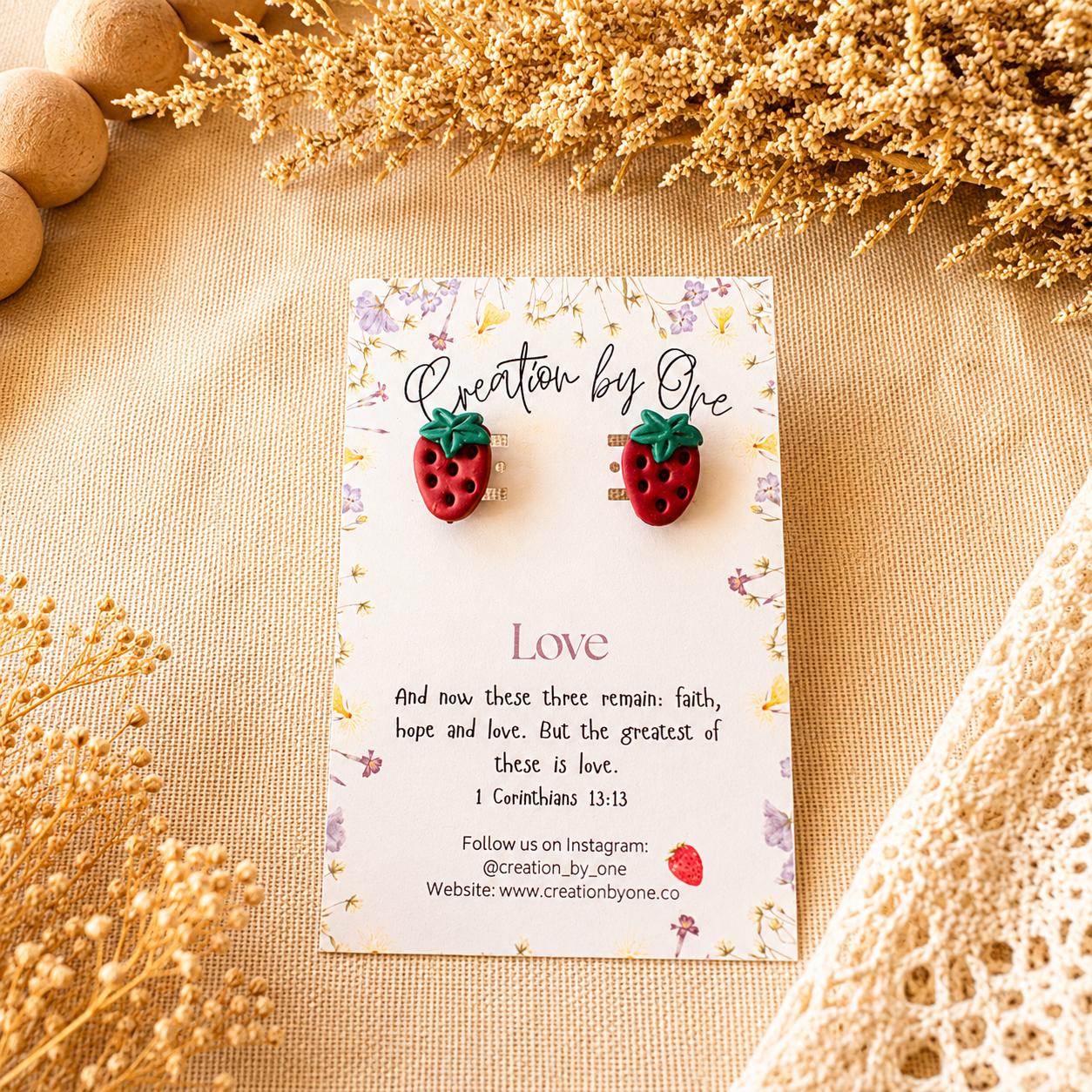 Strawberry-shaped earrings on a card with text and decorative elements on a beige surface.
