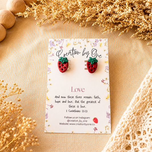 Strawberry-shaped earrings on a card with text and decorative elements on a beige surface.