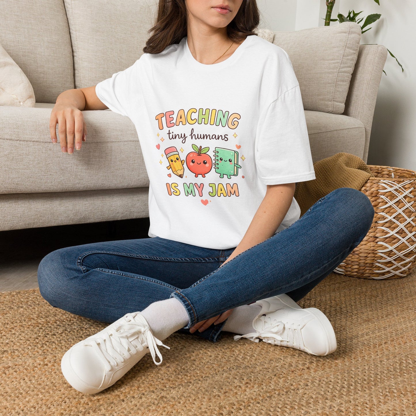 Person sitting on the floor wearing a white t-shirt with a design, blue jeans, and white sneakers in a living room.