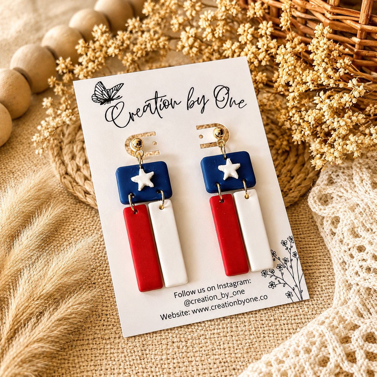 Pair of earrings on a 'Creation by One' branded card with decorative background