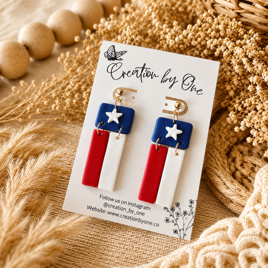 Pair of earrings on a 'Creation by One' branded card with decorative elements.