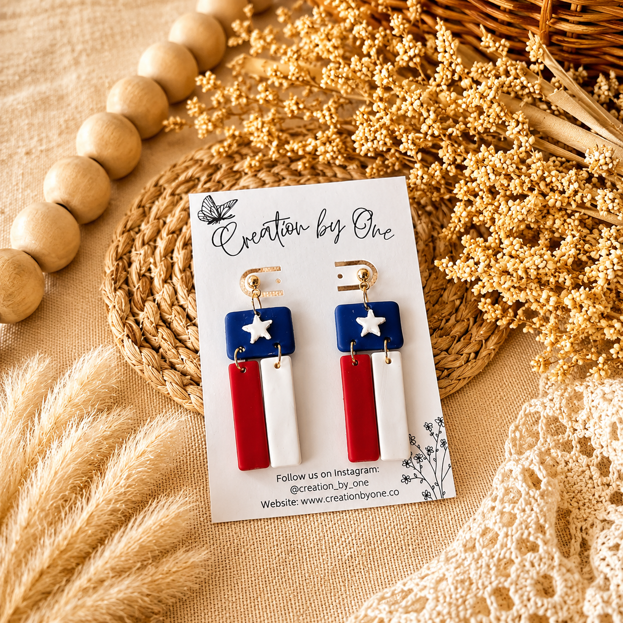 Pair of earrings on a card with 'Creation by One' branding, surrounded by decorative elements.