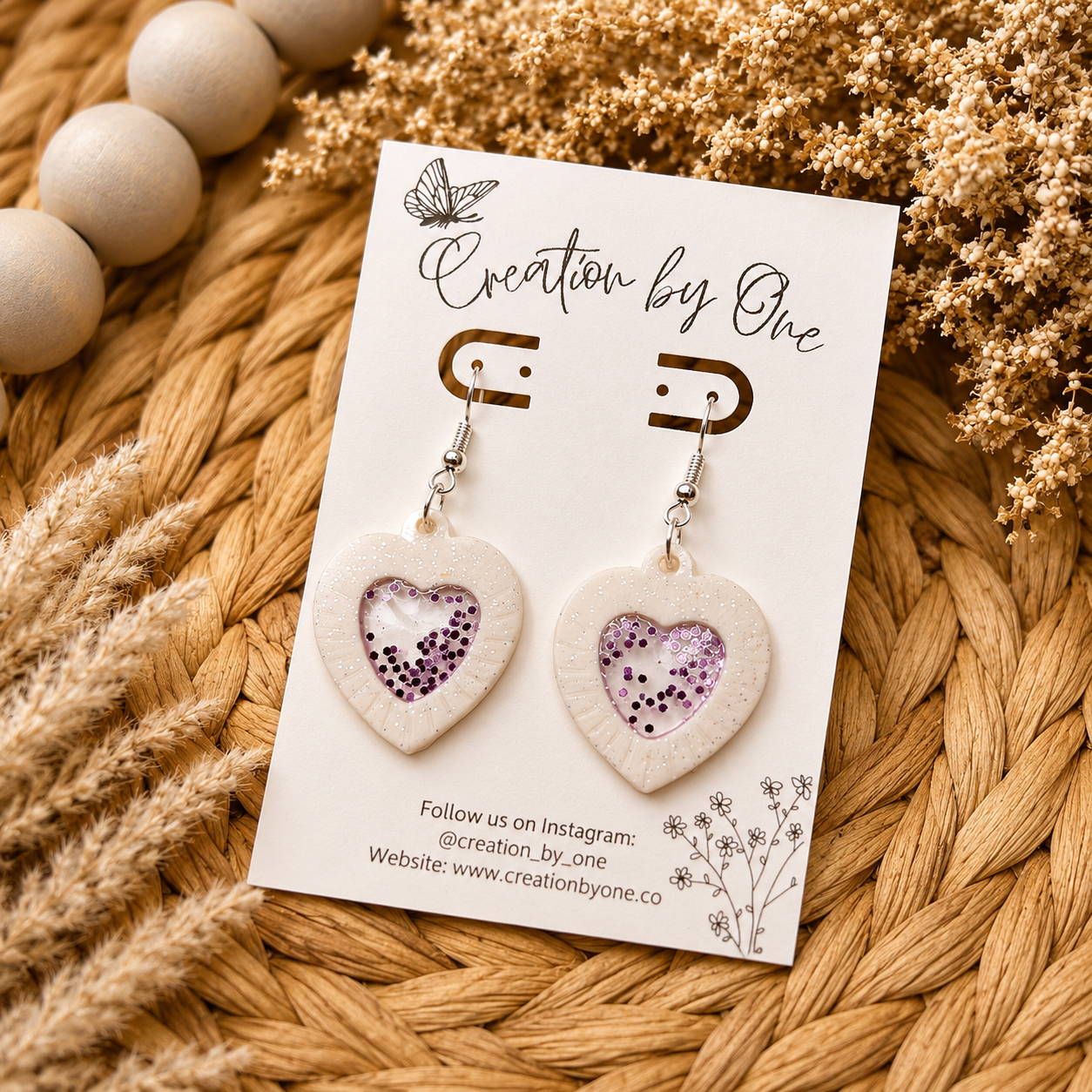 Heart-shaped earrings on a 'Creation by One' branded card with decorative elements.