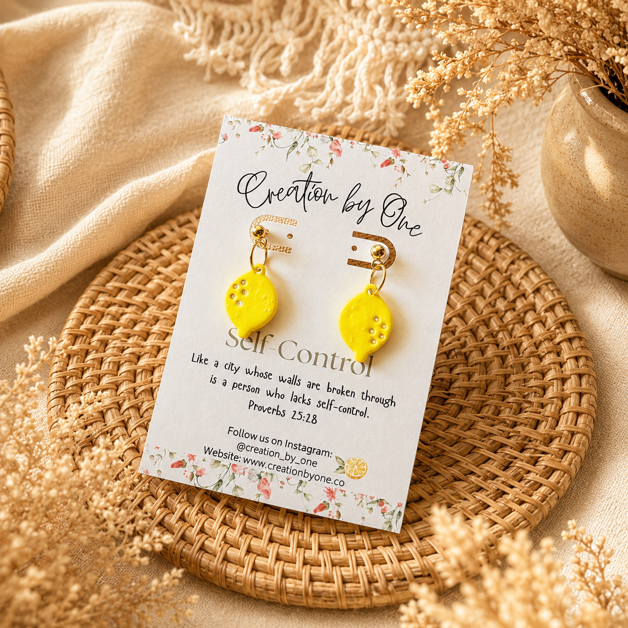 Yellow earrings on a 'Creation by One' branded card with decorative elements on a textured surface.